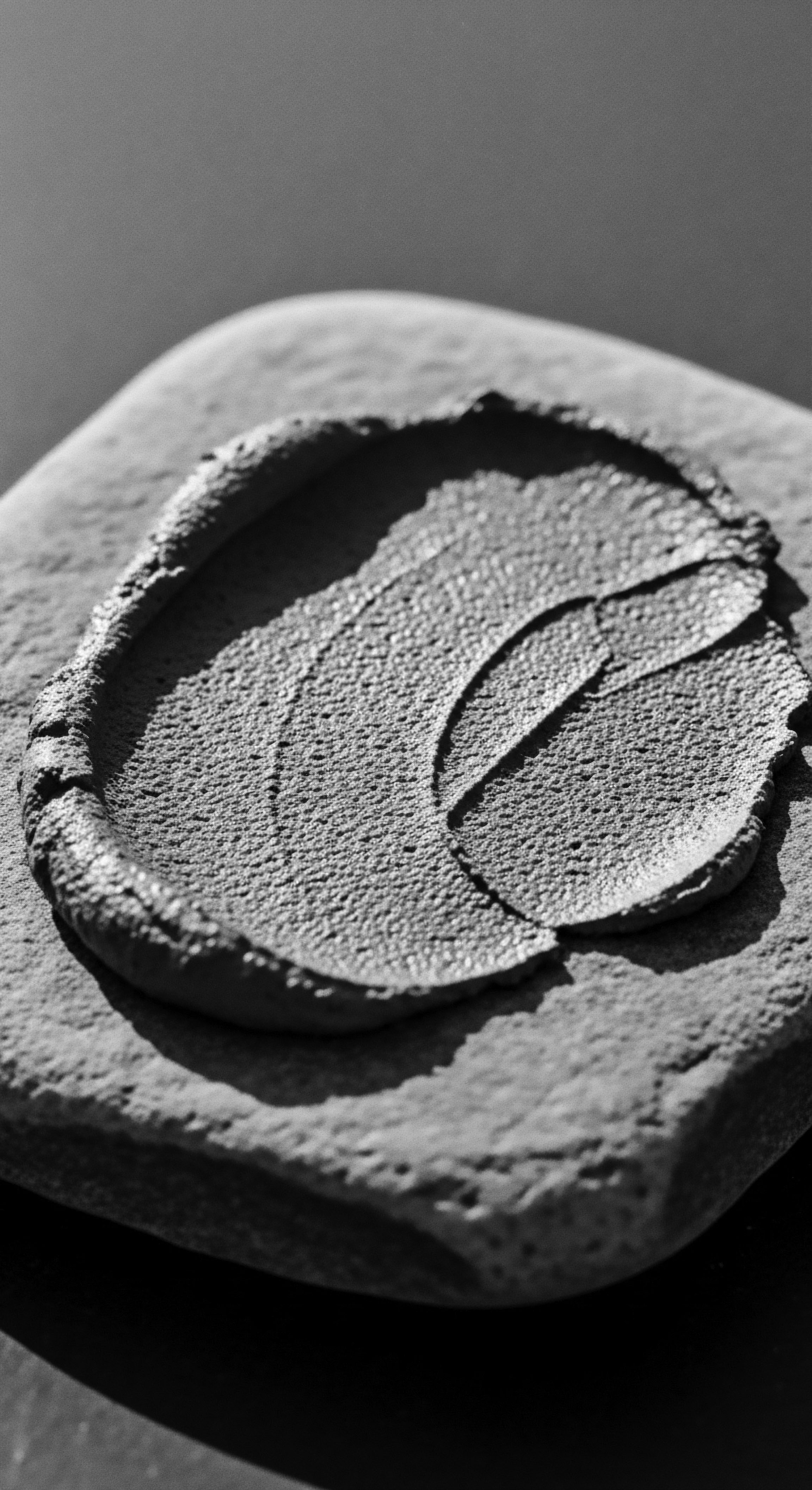 A monochromatic view presents a concentrated portion of a textured clay mask, layered artfully on stone. Light dances across the granular surface, highlighting the careful application with intentional sweeps and swirls. This embodies deep cleansing rituals essential for textured hair's unique needs in holistic care.