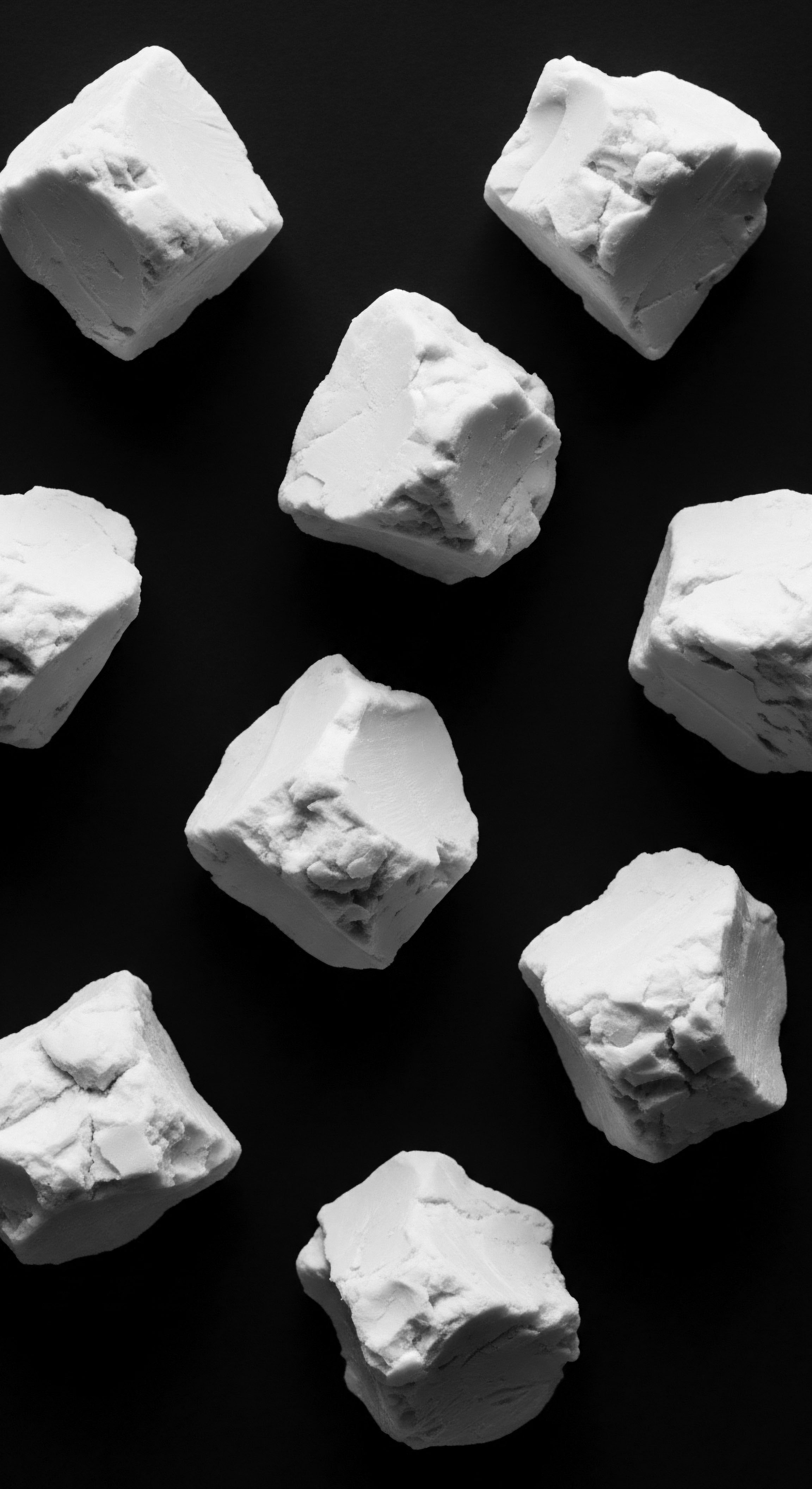 Nine blocks of white solid ingredients, potential components for textured hair formulations like bentonite clay or shea butter, are presented against a stark black field. The monochromatic palette accentuates the varied textures of the blocks, reminiscent of ancestral methods of ingredient processing for holistic hair care.